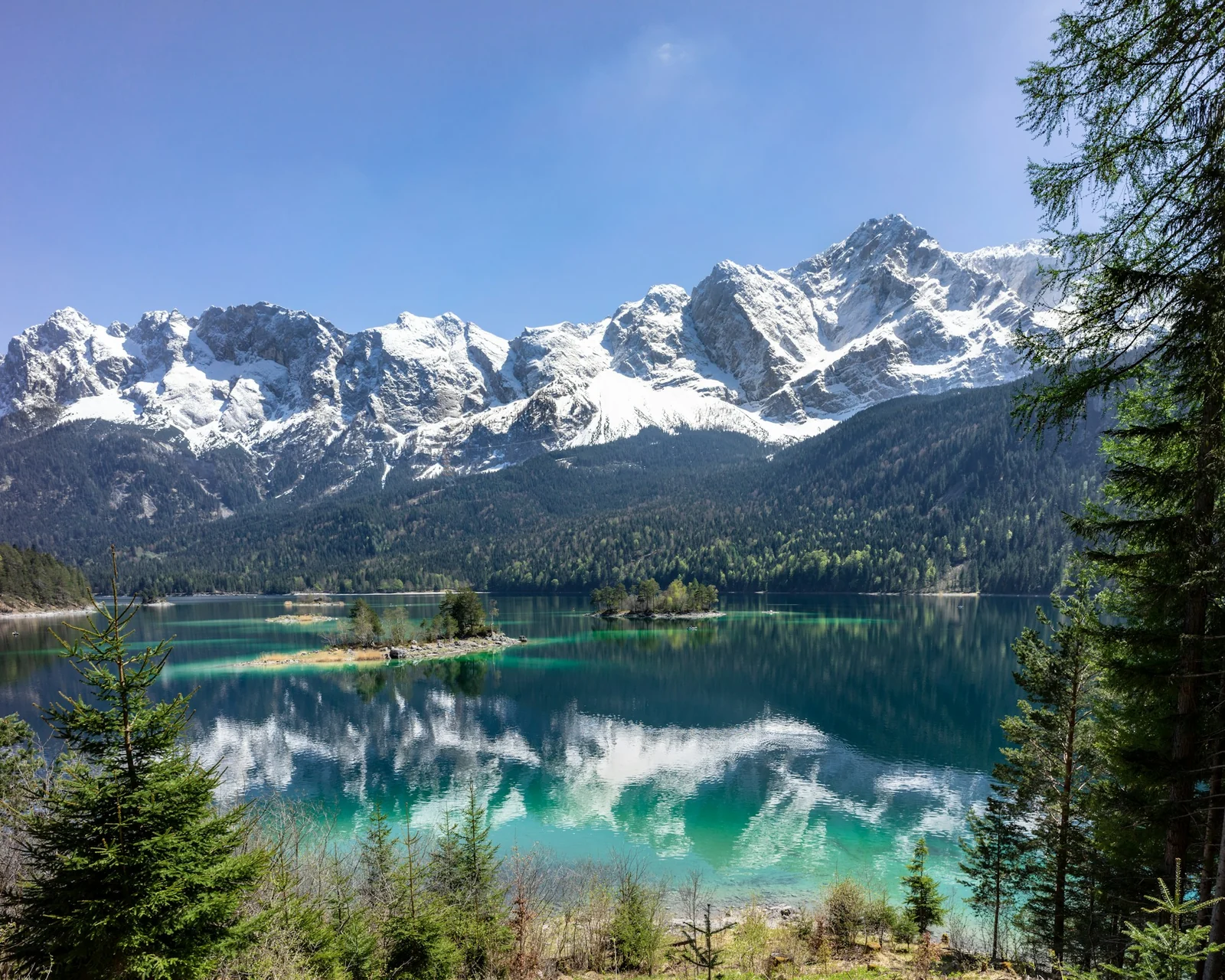Berggipfel und Nadelwald spiegeln sich im ruhigen Eibsee.