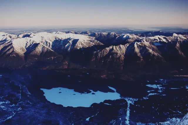 Schneebedeckte Alpengipfel und der winterliche Eibsee aus großer Höhe.