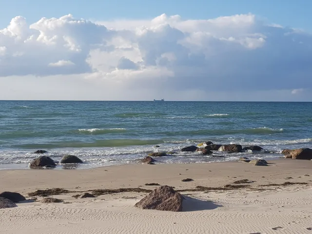 Sandstrand mit Steinen und kleinen Wellen an der Ostsee auf Rügen.
